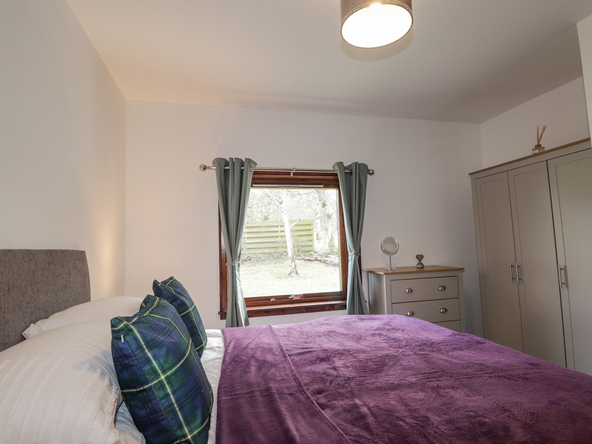 A bedroom with a bed, a dresser, a window with curtains, and a wardrobe.