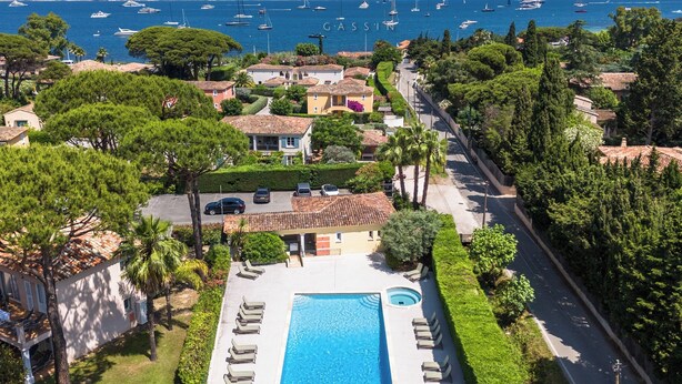 A residential area with a swimming pool, houses, and a view of the sea with boats.