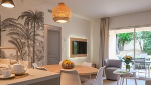 A modern dining area with a round table, white chairs, a fruit bowl, and a television mounted on the wall.
