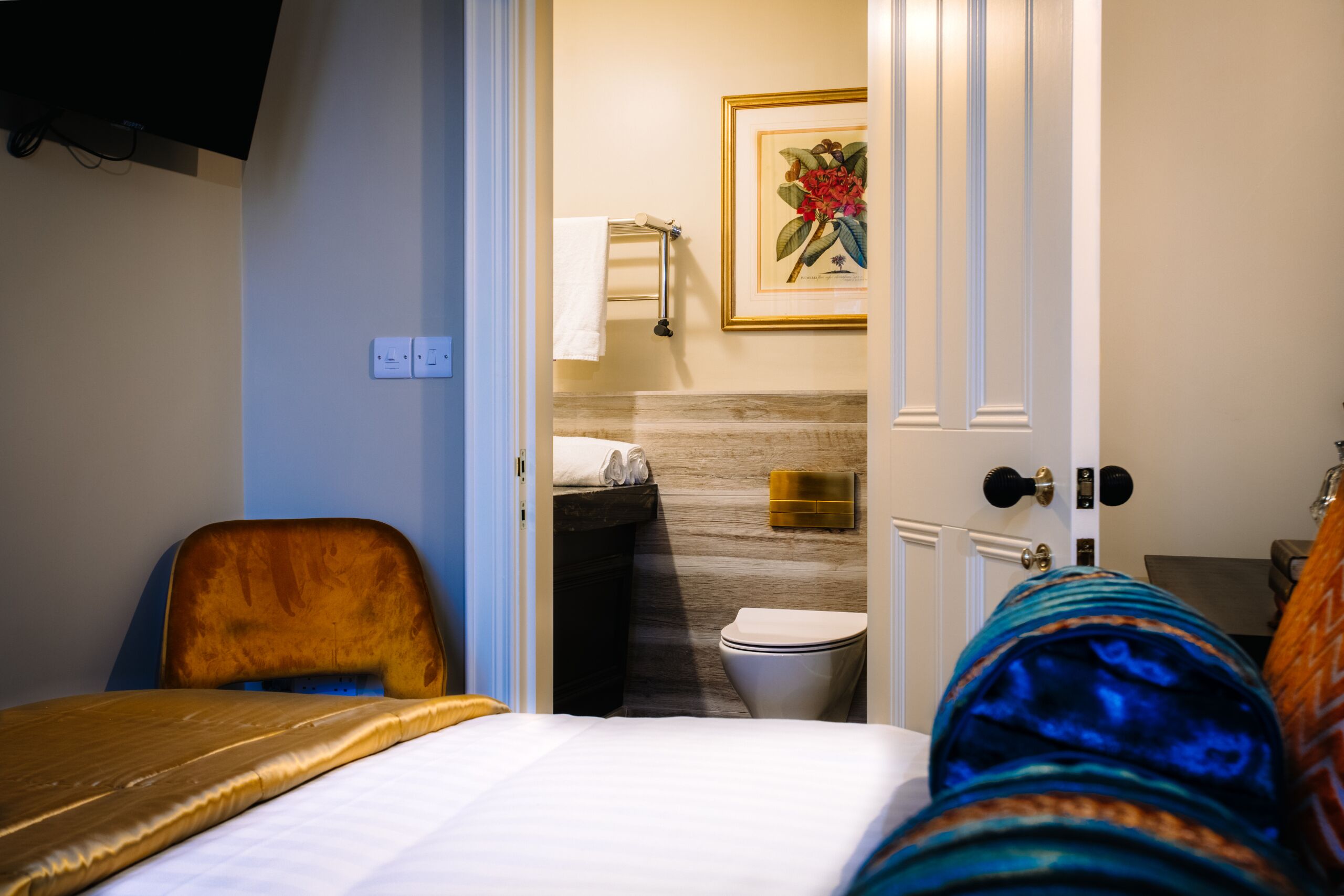 Habitación de hotel con cama, una silla, baño con inodoro, lavamanos y un cuadro en la pared.