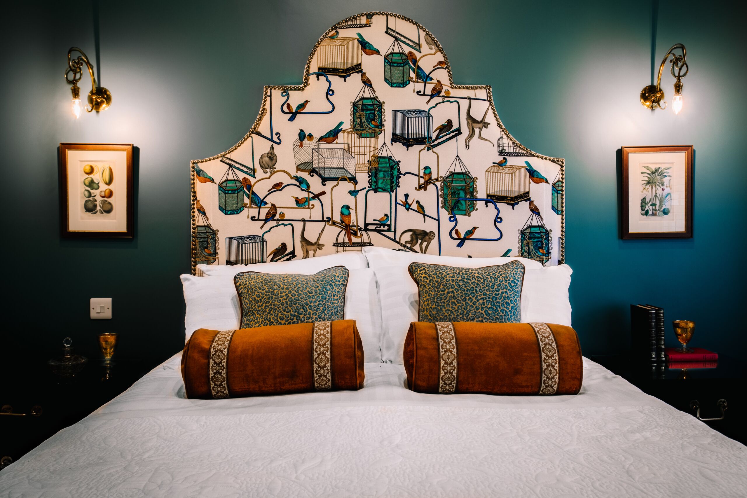 Un dormitorio con una cama grande, dos mesitas de noche, una lámpara de pared y obras de arte enmarcadas.