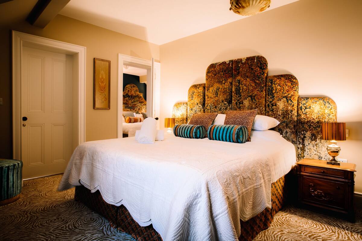 A bedroom with a large bed, a nightstand, a lamp, and a door.