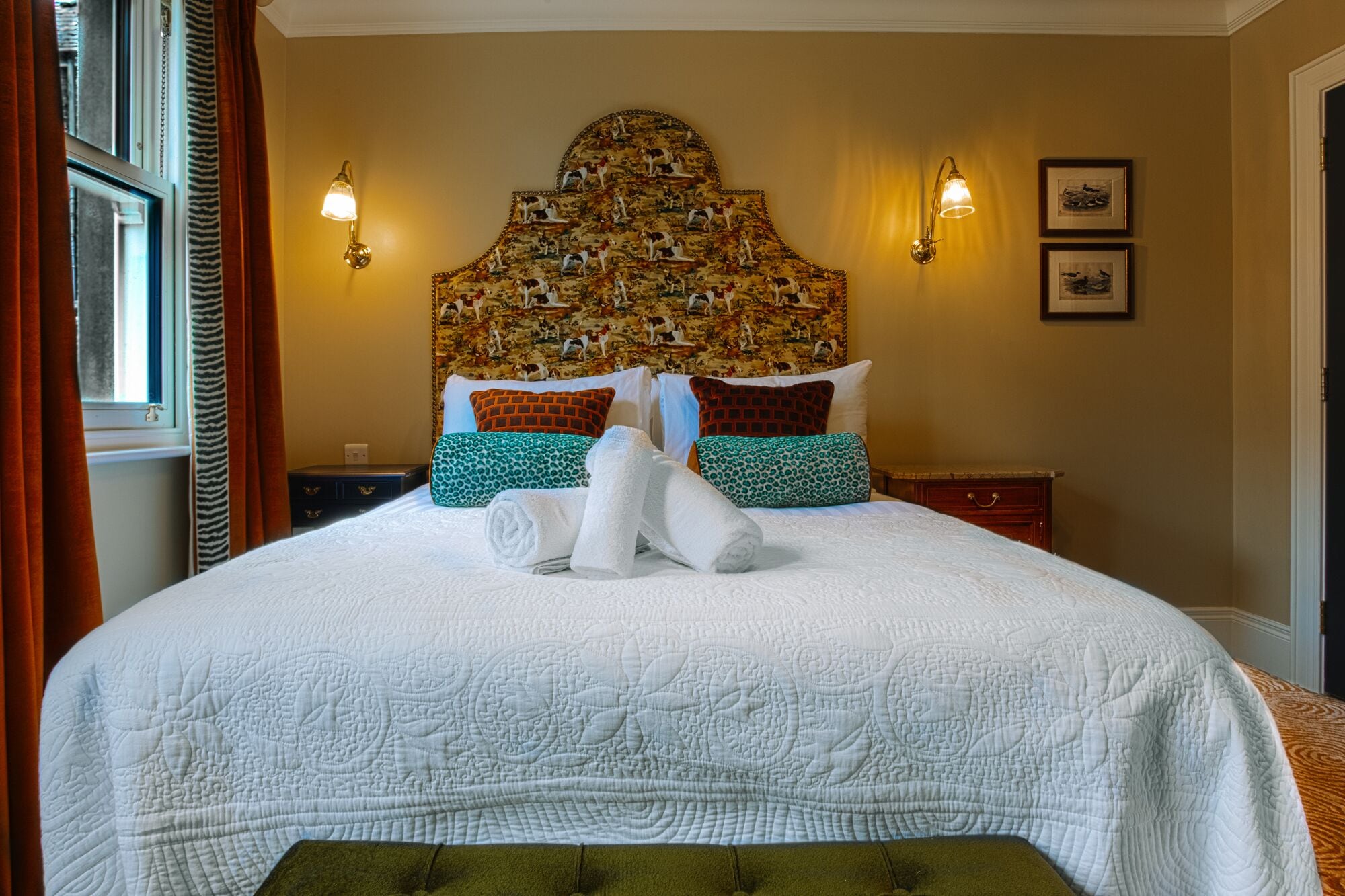 A neatly made bed with a quilted white cover, two wall-mounted lamps, and a headboard with a detailed animal print.