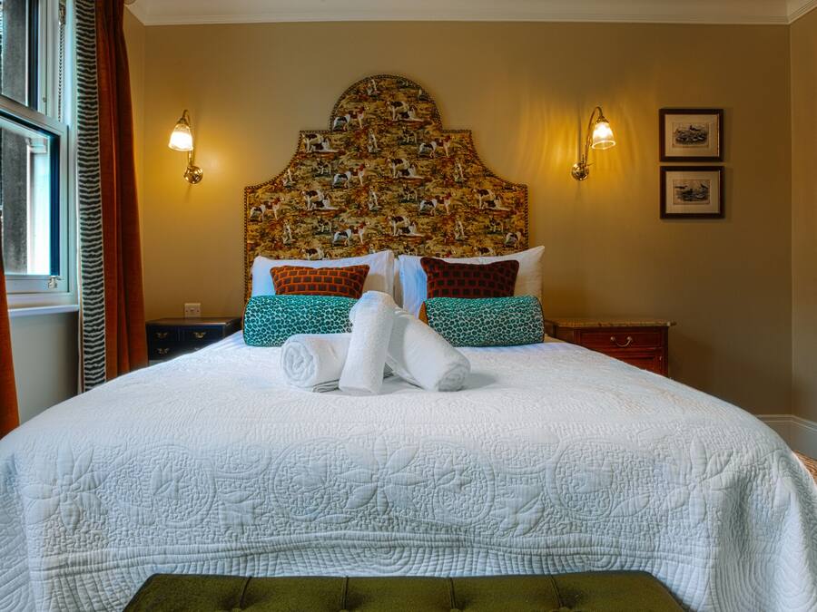 A neatly made bed with a quilted white cover, two wall-mounted lamps, and a headboard with a detailed animal print.