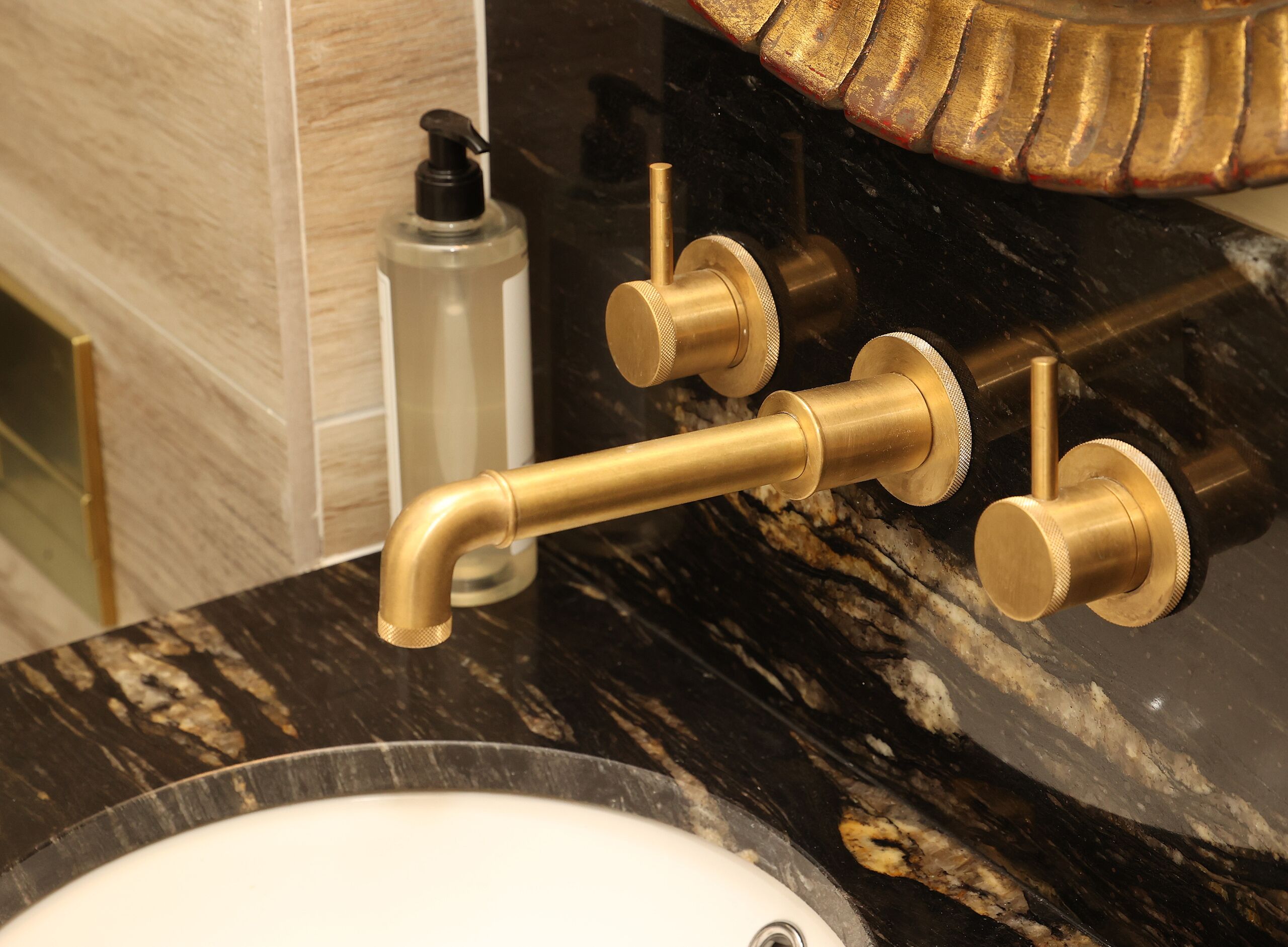 A bathroom with a gold faucet, a soap dispenser, and a marble countertop.