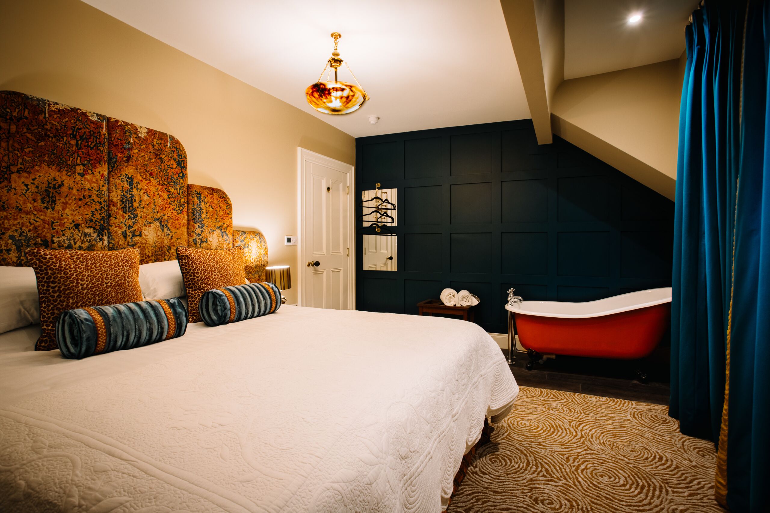 A bedroom with a large bed, a red clawfoot bathtub, and a dark accent wall.