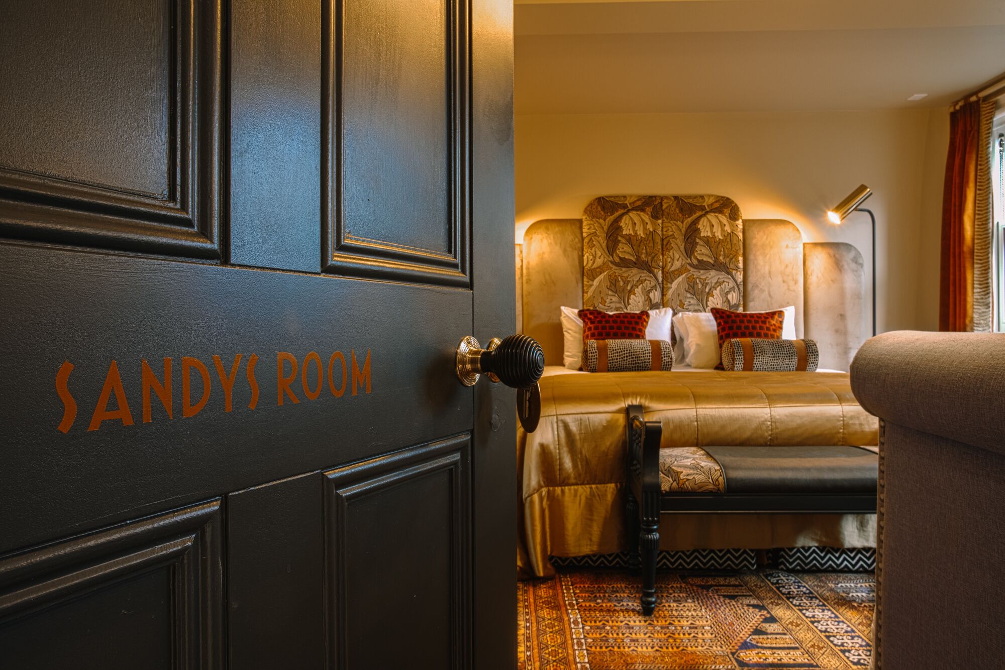 Una habitación con una cama, una silla y una puerta con la leyenda 'SANDYROOM'.