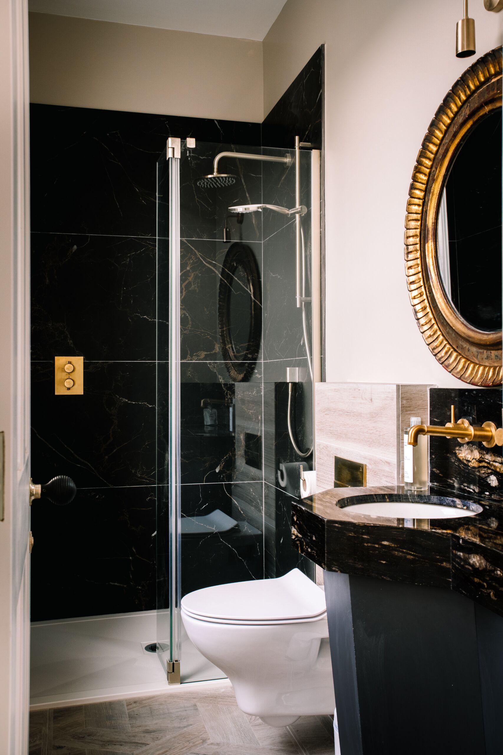 A modern bathroom with a glass-enclosed shower, a white toilet, and a vanity with a gold-framed mirror.