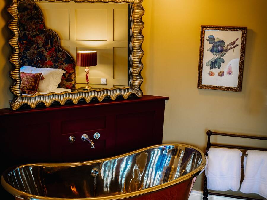Ein Badezimmer mit einer großen, verzierten Badewanne, einem Spiegel mit dekorativem Rahmen und einer Chandelier.