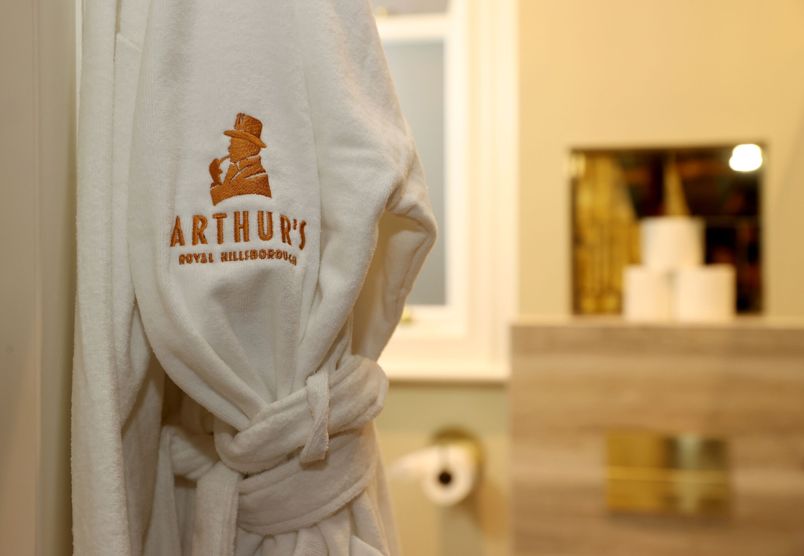 Una bata blanca con el bordado 'ARTHUR'S ROYAL HILLSBOROUGH'.