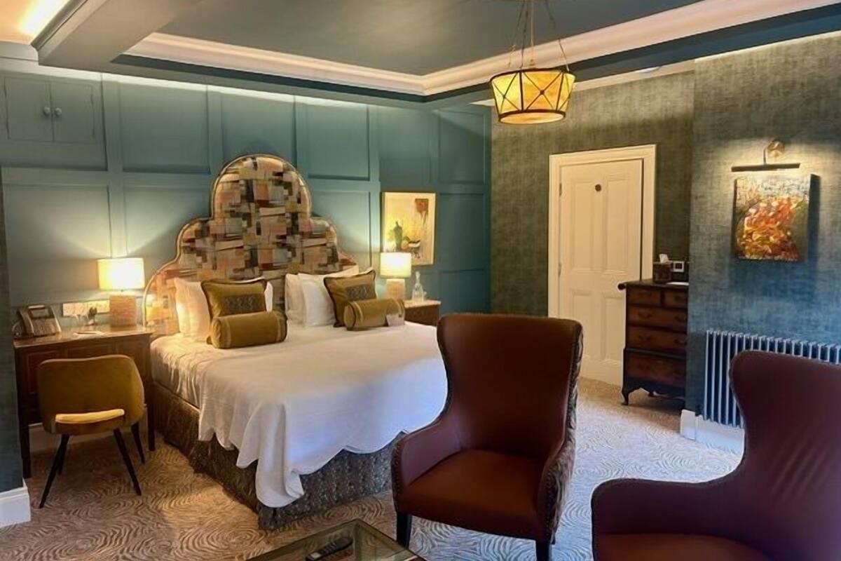 A bedroom with a large bed, two chairs, a dresser, and a painting on the wall.