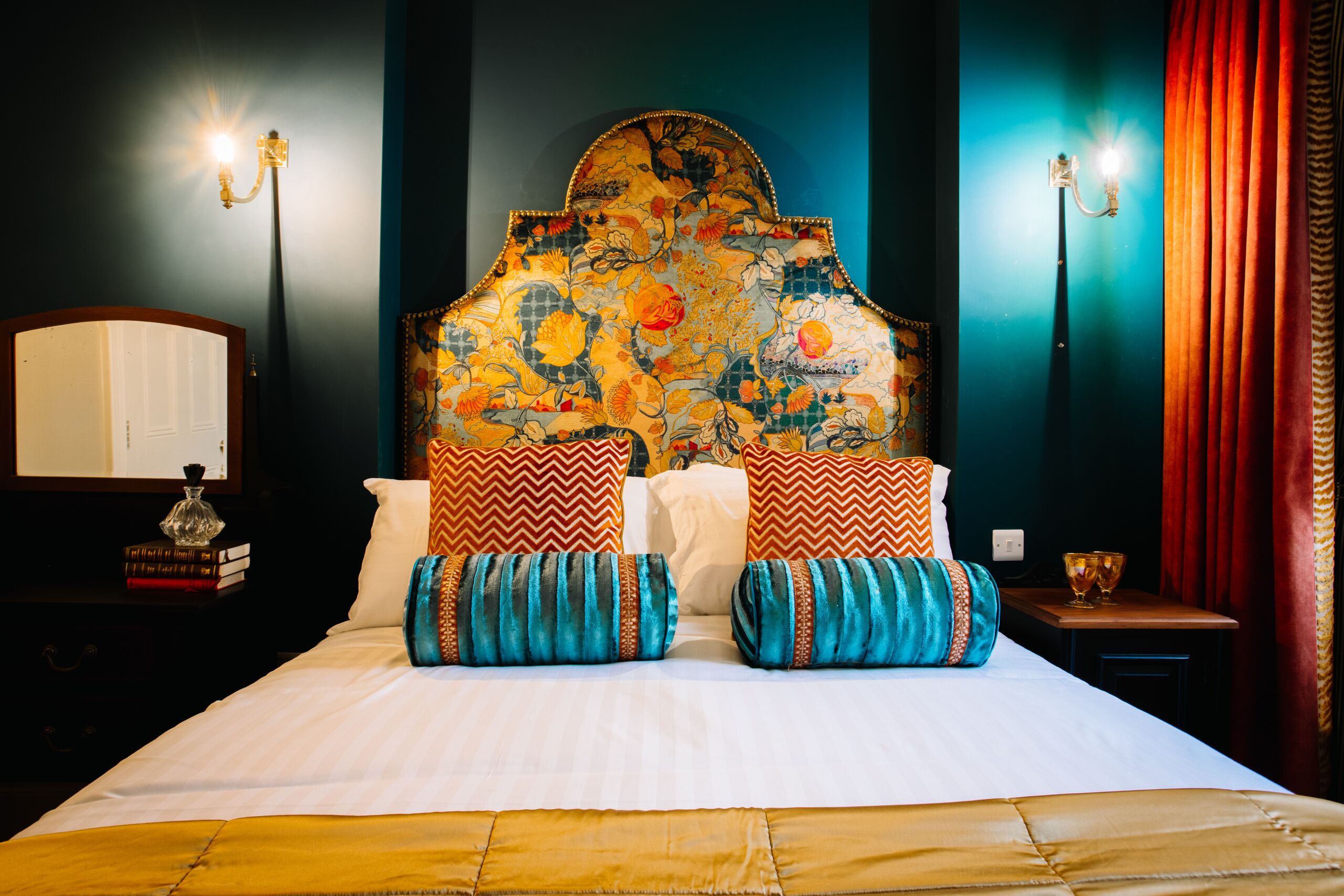 Una cama con cabecera estampada, ropa de cama blanca y almohadones decorativos.