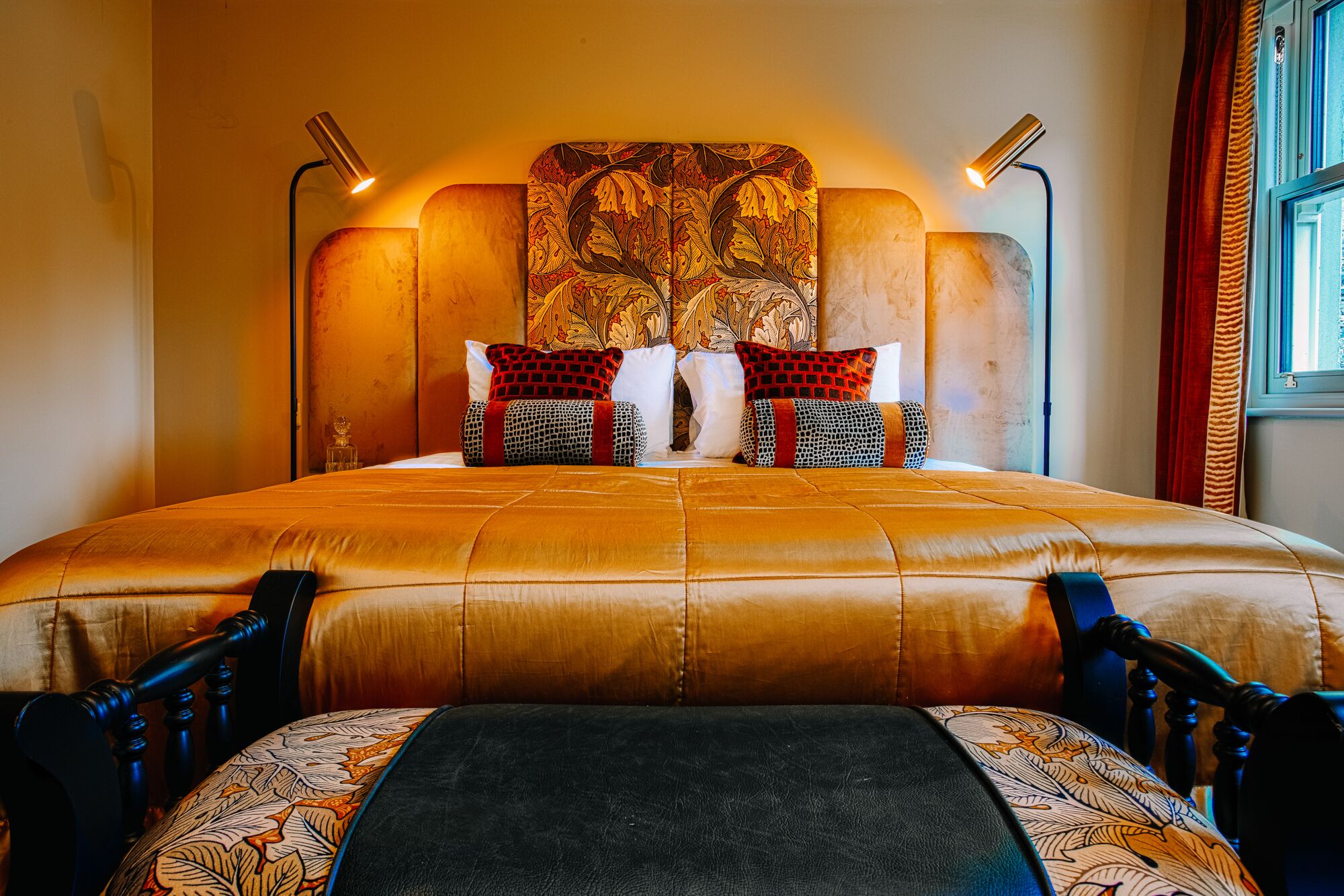 Una cama grande con cabecera estampada, dos lámparas de noche y una ventana con cortinas.