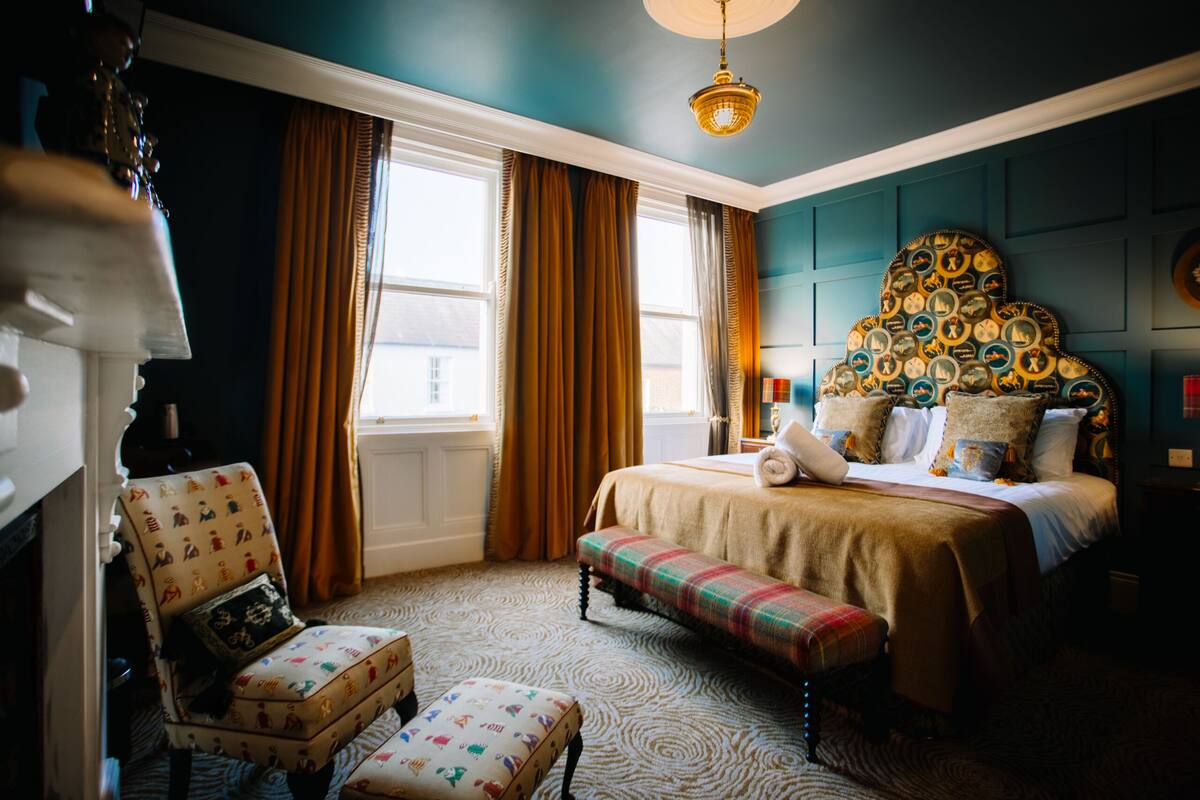 A bedroom with a large bed, a bench, a chair, and a fireplace.