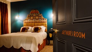 Une chambre à coucher avec un lit, une tête de lit, une table de chevet et une porte portant l’inscription « CHAMBRE D’ARTHUR ».