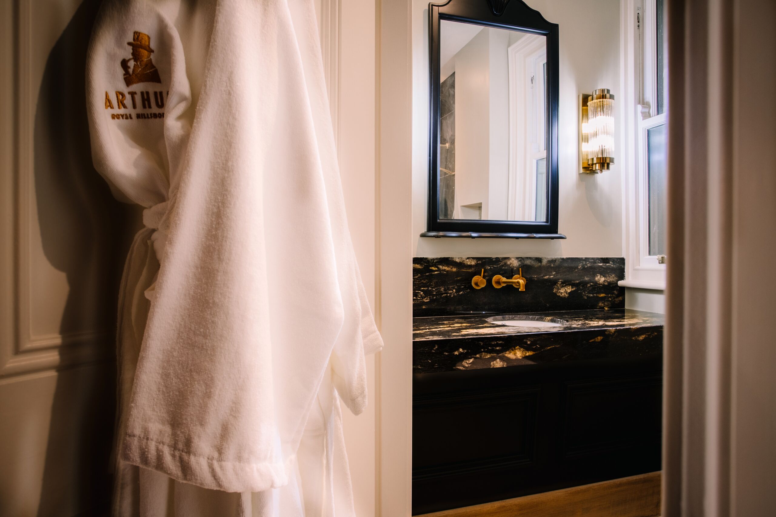 Un baño con una toalla blanca colgada en un perchero, un lavabo de mármol negro y un espejo encima.