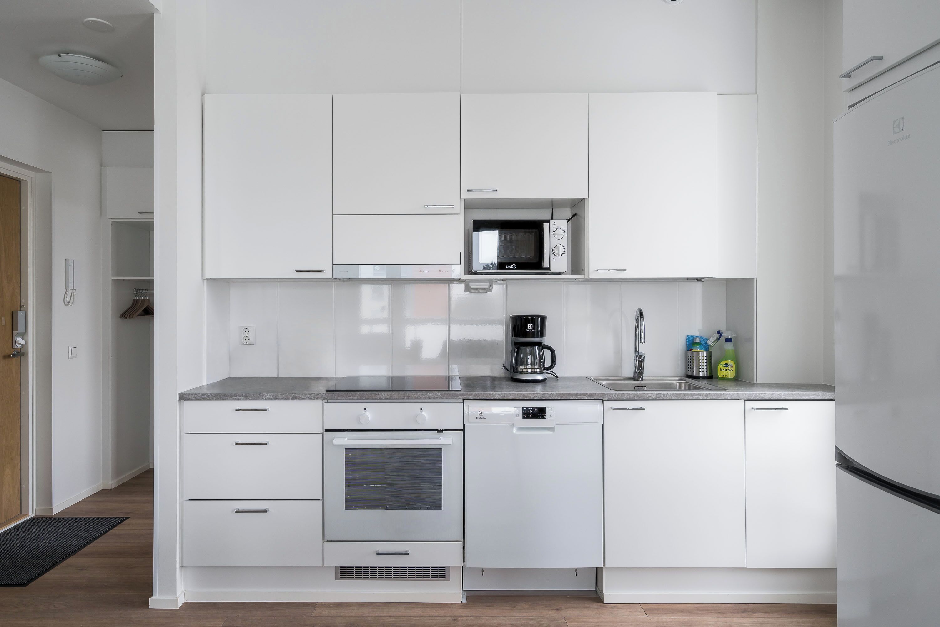 A modern kitchen with white cabinetry, a built-in microwave, a coffee maker, and a dishwasher.