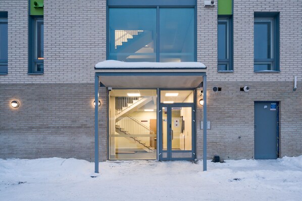 Een gebouwde ingang met een glazen deur, een wenteltrap naar binnen, en een met sneeuw bedekte grond.