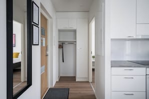 Une cuisine moderne avec des meubles blancs, un plancher en bois et un paillasson noir à l’entrée.
