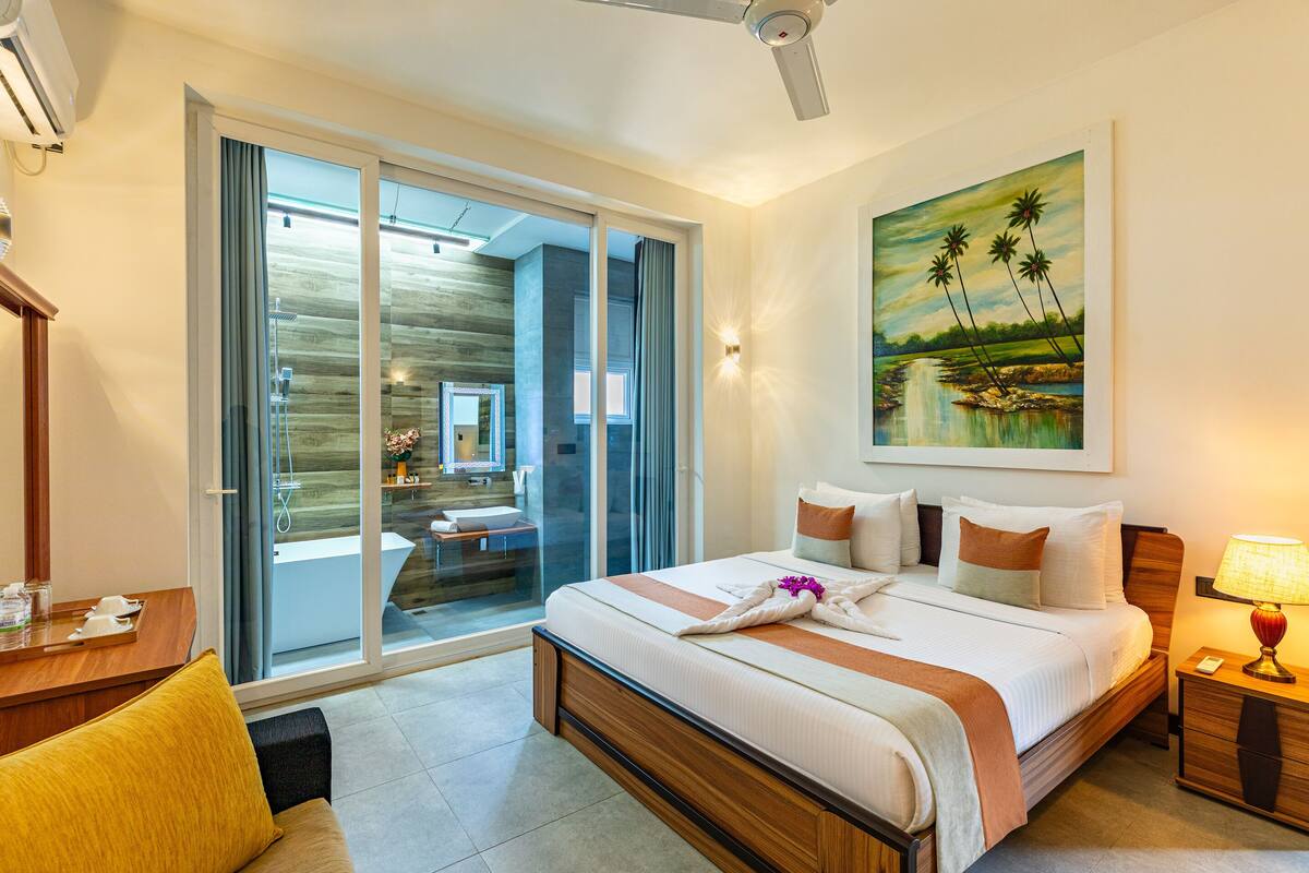 A hotel room with a large bed, a desk, a chair, a nightstand, a lamp, and a painting on the wall.