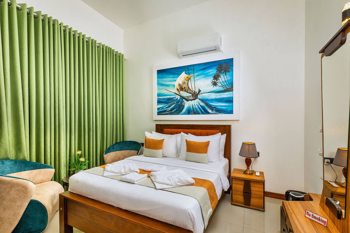 A hotel room with a bed, a nightstand, a chair, a painting of a sailboat, and a 'No Smoking' sign.