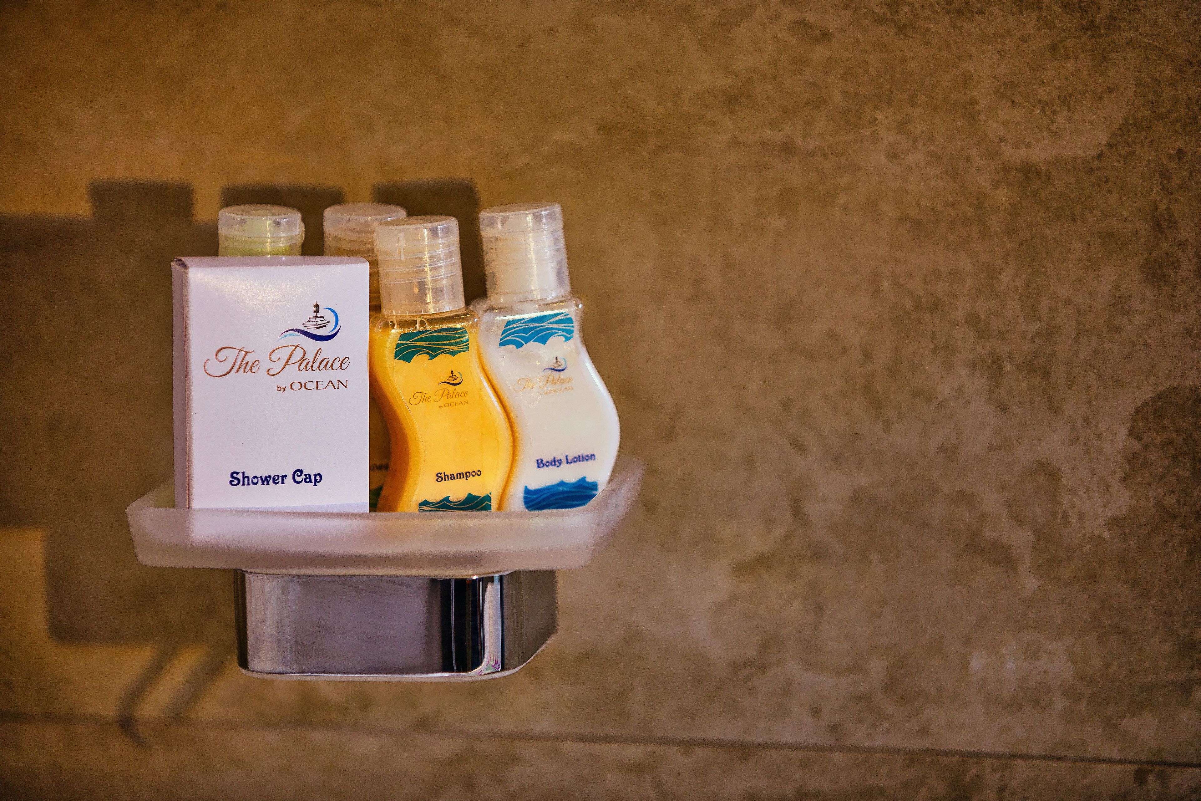 A shower area with a shower cap and bottles of shampoo and body lotion.