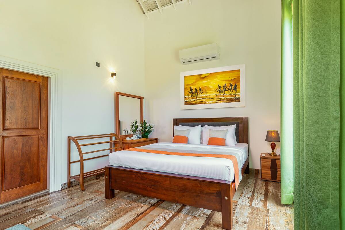 A bedroom with a wooden bed, a nightstand, a lamp, a painting, and a green curtain.