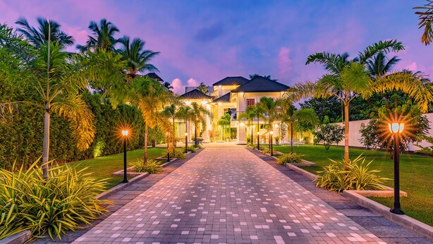 A well-lit pathway leading to a house with a paved entrance, surrounded by palm trees and well-maintained greenery. - The Palace by Ocean (Ahungalla)