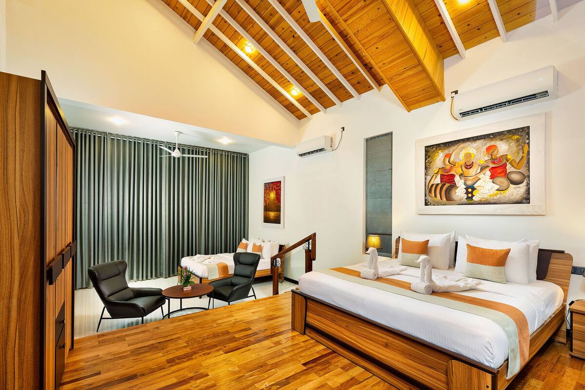A modern hotel room with a wooden ceiling, a large bed with white bedding, a desk with a chair, and a painting on the wall.