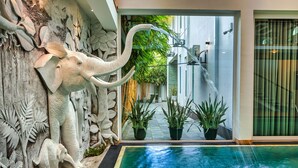 A swimming pool with a water feature, surrounded by a stone wall with elephant carvings and potted plants. - The Palace by Ocean (Ahungalla)