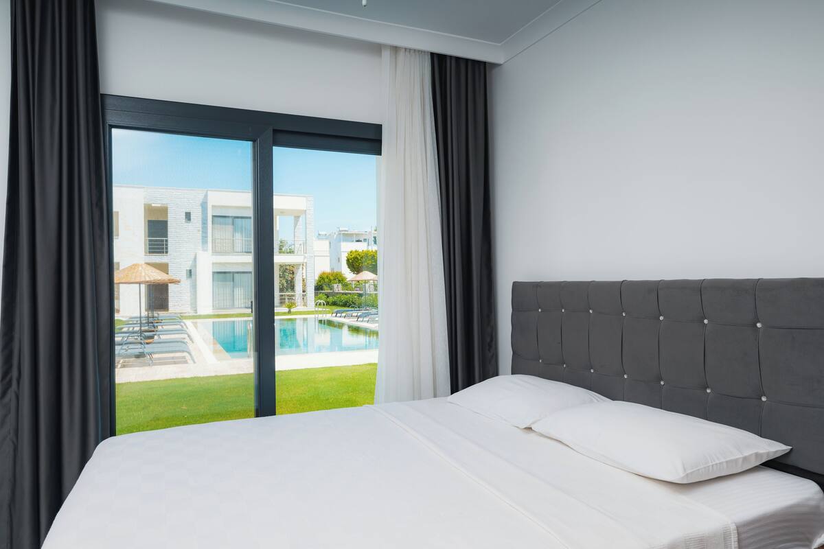 Una habitación de hotel con una cama, vistas a una piscina y un edificio moderno al fondo.