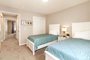 Une chambre avec deux lits, une table de chevet avec une lampe et une porte donnant sur une autre pièce.