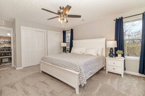A bedroom with a bed, nightstands, a ceiling fan, a window with curtains, and a view of the outdoors.