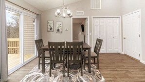 Uma sala de jantar com mesa e cadeiras, um lustre e vista para o deck.