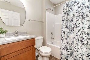 Une salle de bain équipée d’un WC, d’un lavabo, d’un miroir, d’une douche et d’un rideau de douche à motifs floraux.