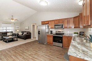 Ein geräumiges Wohnzimmer mit Kamin, eine Küche mit Holzschränken und Edelstahlgeräten sowie ein Essbereich mit Marmorplatte.