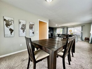 A dining area with a large wooden table and six chairs, a world map artwork on the wall, and a kitchen visible through an open doorway. - 6268 Mullen · Among trees outside the city (Cincinnati)