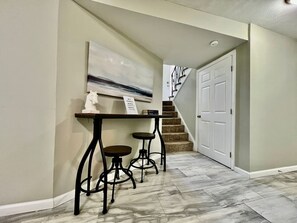 A hallway with a staircase, a white door, and a table with two stools. - 6268 Mullen · Among trees outside the city (Cincinnati)