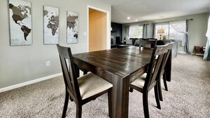 Comedor con una gran mesa de madera y sillas, una cocina al fondo y un cuadro con un mapa del mundo en la pared.