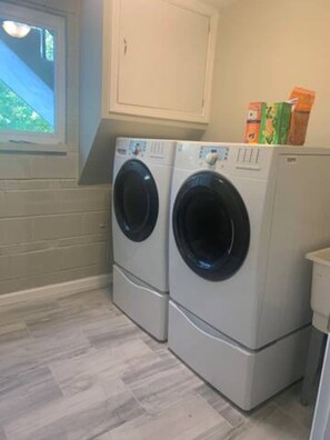 A laundry room with two front-loading washing machines and a window. - 6268 Mullen · Among trees outside the city (Cincinnati)