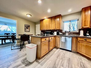 A modern kitchen with wooden cabinets, a dishwasher, and a dining area with a table and chairs. - 6268 Mullen · Among trees outside the city (Cincinnati)