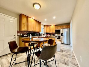 A modern kitchen with wooden cabinets, a central island with seating, stainless steel appliances, and a white door. - 6268 Mullen · Among trees outside the city (Cincinnati)