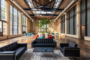 A spacious indoor area with large windows, a central seating area with sofas and a coffee table, and a large potted plant. - 5104 Cartridge Factory Loft (Maineville)