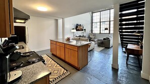 A modern kitchen with a central island, a dining area with a table and chairs, and a living room with a sofa and a coffee table. - 5104 Cartridge Factory Loft (Maineville)