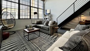 A spacious living room with a large window, a sofa, a coffee table, and a hanging chair. - 5104 Cartridge Factory Loft (Maineville)