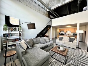 Un espace de vie moderne comprenant un canapé d’angle, une table basse, une bibliothèque et un escalier menant à un niveau supérieur.