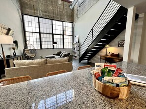 A spacious kitchen with a granite countertop, a wicker sofa, and a staircase leading to an upper level. - 5104 Cartridge Factory Loft (Maineville)