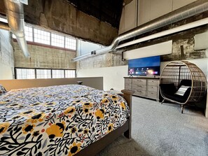Une chambre moderne avec un grand lit, un fauteuil suspendu et une vue sur la ville.