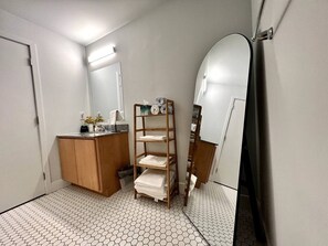 A bathroom with a tiled floor, wooden cabinets, a shelf with towels, and a mirror.