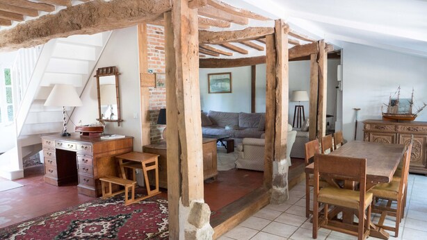 Una habitación rústica con vigas de madera a la vista, una pared de ladrillo, una mesa de madera con sillas, un sofá y un aparador.